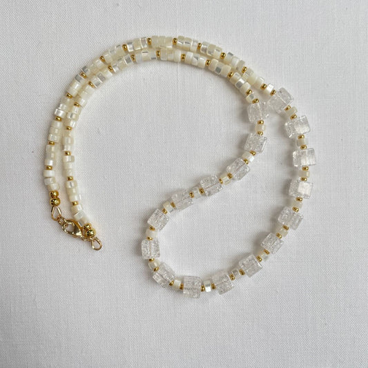 Deze ketting met een zachte uitstraling is gemaakt van bergkristal cubes van 6 mm en parelmoer heishi kralen afgewisseld met kleine 24K goldplated kraaltjes. De ketting is 43 cm en sluit met een 14K gold filled slotje.
