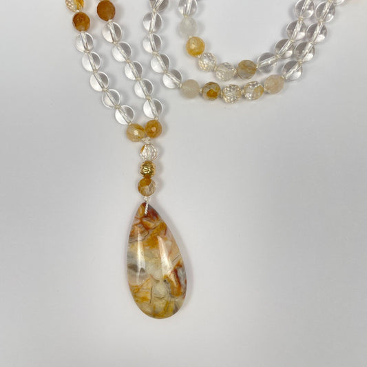 Mala ketting van bergkristal en golden healer kralen met een hanger van een gold filled kraal en een druppelvormige agaat in gele en bruine kleuren. Hier zie je de kleuren van de hanger: lichtbruin, geel en beige.