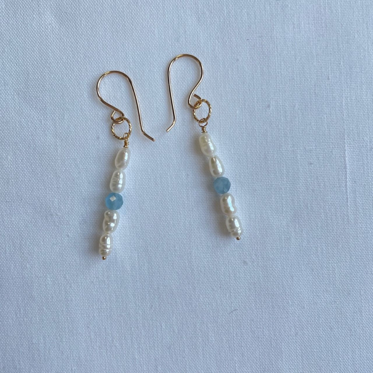 Aan een 14K gold filled haakje hangt aan een bewerkt ringetje een bedel van een aquamarijn facetkraaltjes en zoetwaterparels.