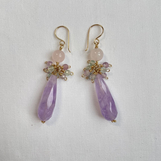 Aan een 14K gold filled haakje hangt een lange facetdruppel van lavendel amethist. Daarboven een rozenkwarts kraal en een trosje fluoriet facetkraaltjes in zachtgroene en paarse kleurtjes.