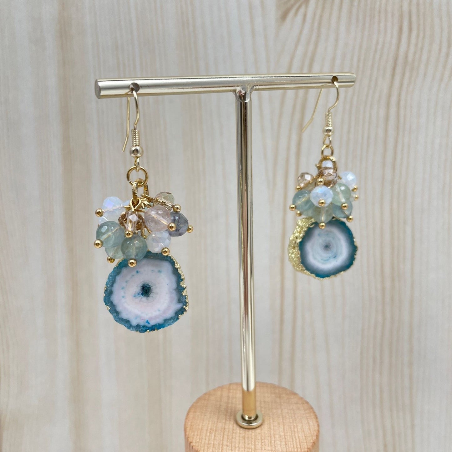 Aan een 14K gold filled haakje hangt een blauw ingekleurde druzy agaat met daarboven een trosje kralen van kristal en fluoriet in de kleuren van de agaat. De agaat heeft een goldplated randje.