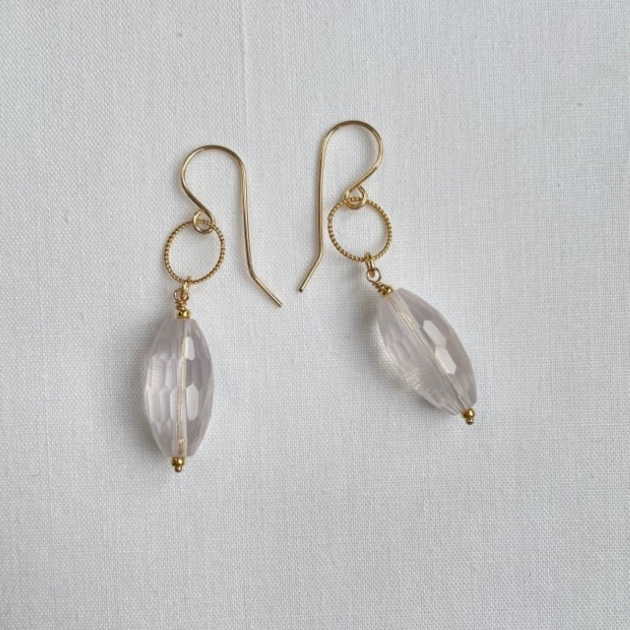 Aan een 14K gold filled haakje met ook nog een bewerkte 14K goldfilled ring, hangt een transparante rozenkwarts druppel. De druppel is facet geslepen, zodat deze mooi het licht vangt.